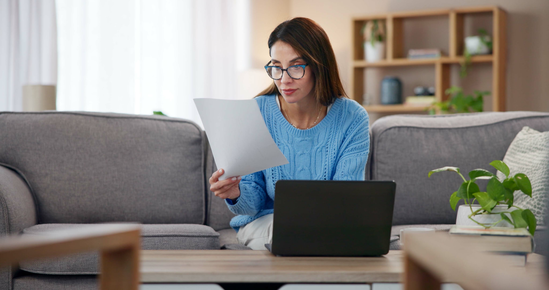 Eine Frau liest zuhause nachdenklich ein Dokument, neben ihr der Laptop